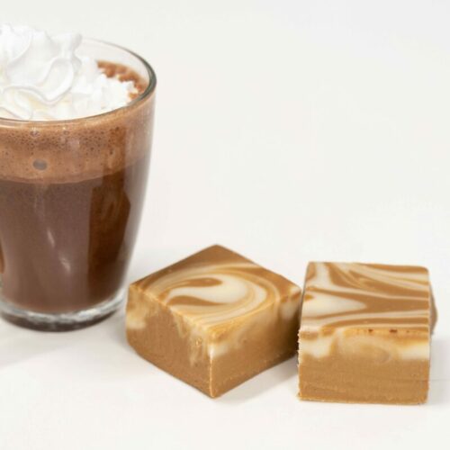 Two pieces of Cappuccino Fudge photographed with a clear glass of cappuccino with whip cream on top.