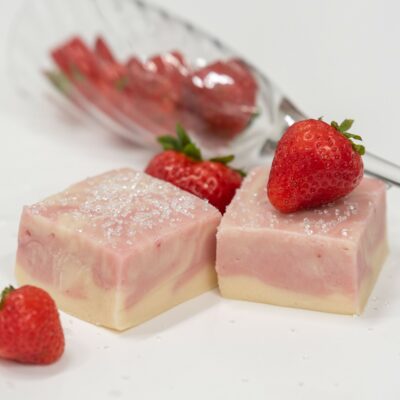 Two pieces of Strawberry Champagne Fudge photographed with full strawberries and a champagne glass.