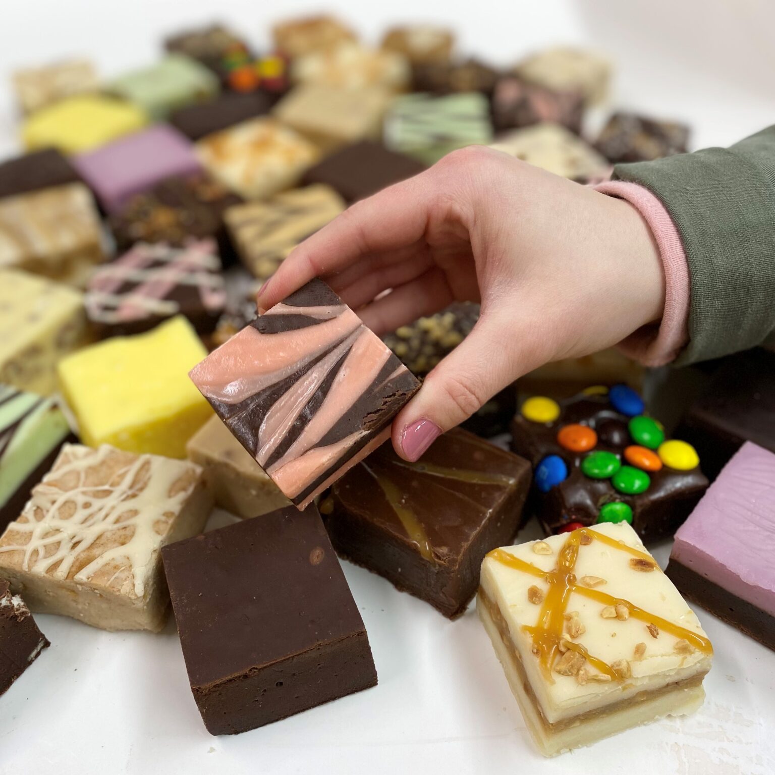 4 oz. piece of Amaretto Chocolate Fudge in hand with assorted fudge pieces in the background.