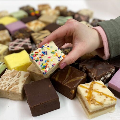 4 oz. piece of Birthday Cake Fudge in hand with assorted fudge pieces in the background.