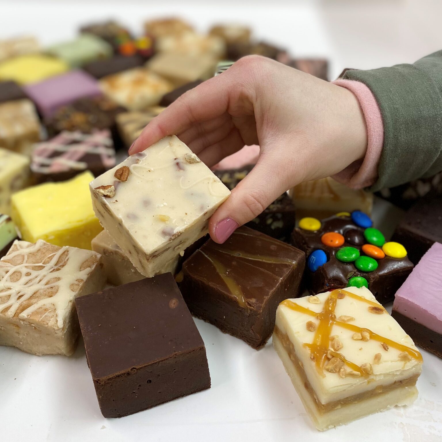 4 oz. piece of Bourbon Maple Pecan Fudge in hand with assorted fudge pieces in the background.