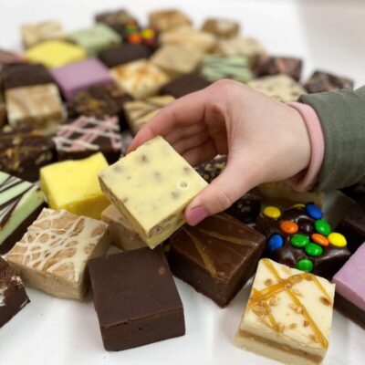 4 oz. piece of Butter Pecan Fudge in hand with assorted fudge pieces in the background.