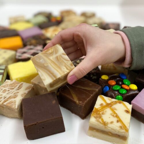 4 oz. piece of Cappuccino Fudge in hand with assorted fudge pieces in the background.