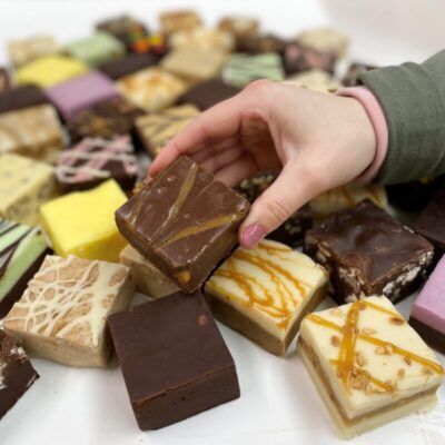 4 oz. piece of Caramel Chocolate Fudge in hand with assorted fudge pieces in the background.