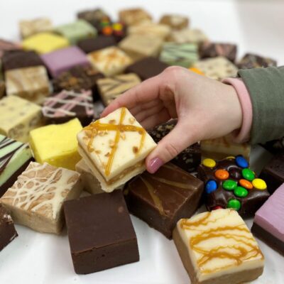 4 oz. piece of Caramel Salted Peanut Fudge in hand with assorted fudge pieces in the background.