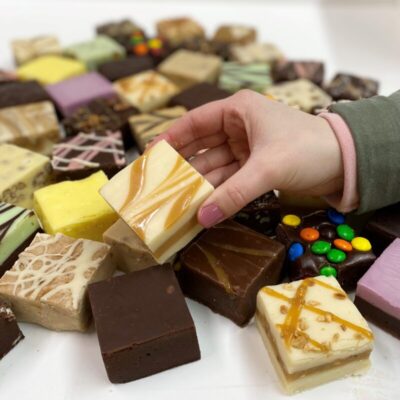 4 oz. piece of Caramel Vanilla Swirl Fudge in hand with assorted fudge pieces in the background.