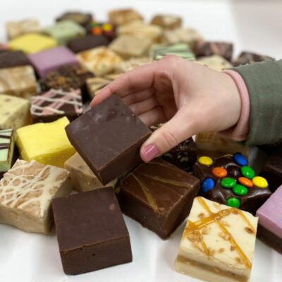 4 oz. piece of Chocolate Fudge in hand with assorted fudge pieces in the background.