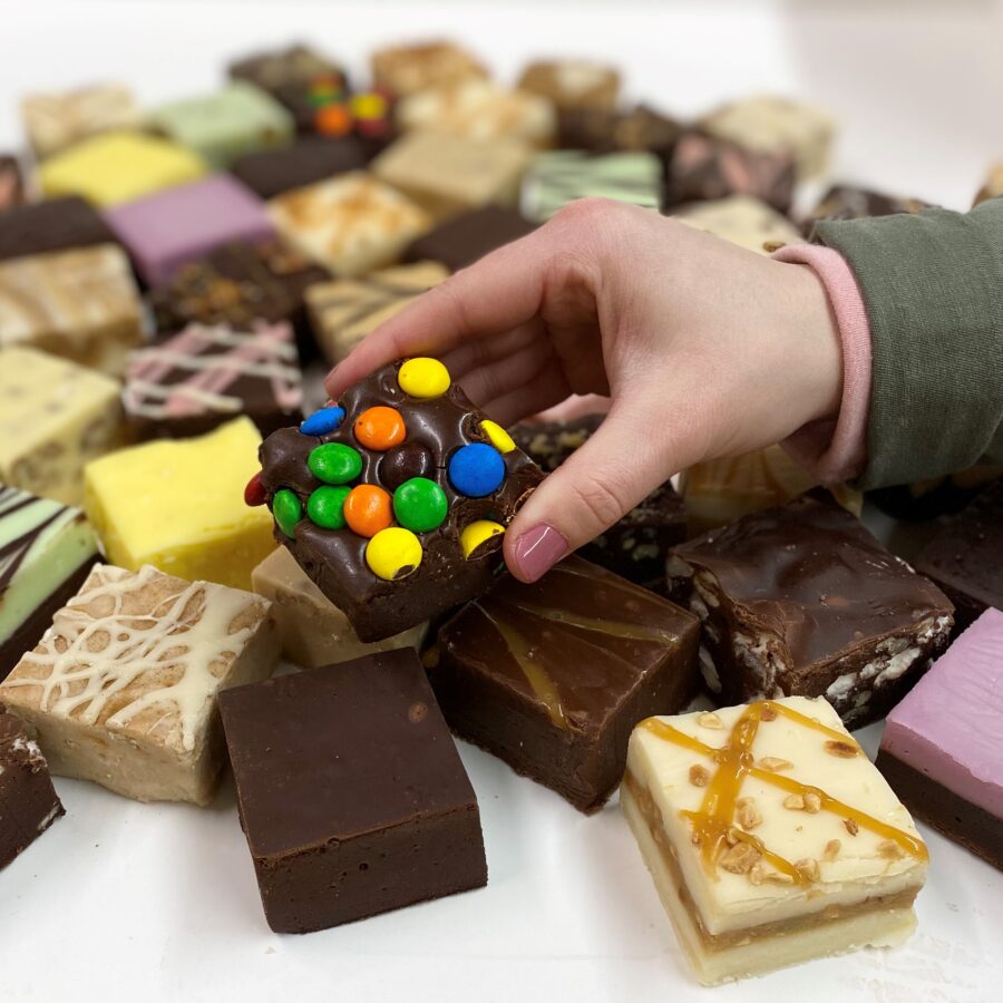 4 oz. piece of Chocolate Fudge with M&M's in hand with assorted fudge pieces in the background.