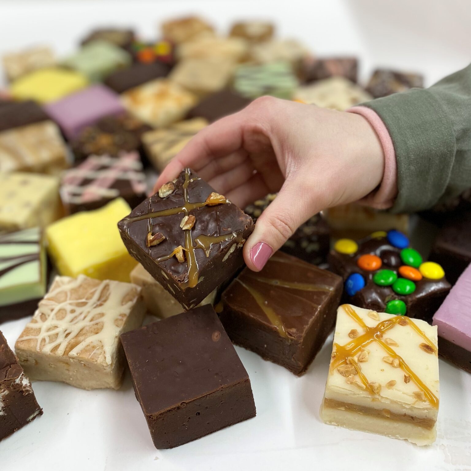 4 oz. piece of Chocolate Pecan Turtle Fudge in hand with assorted fudge pieces in the background.