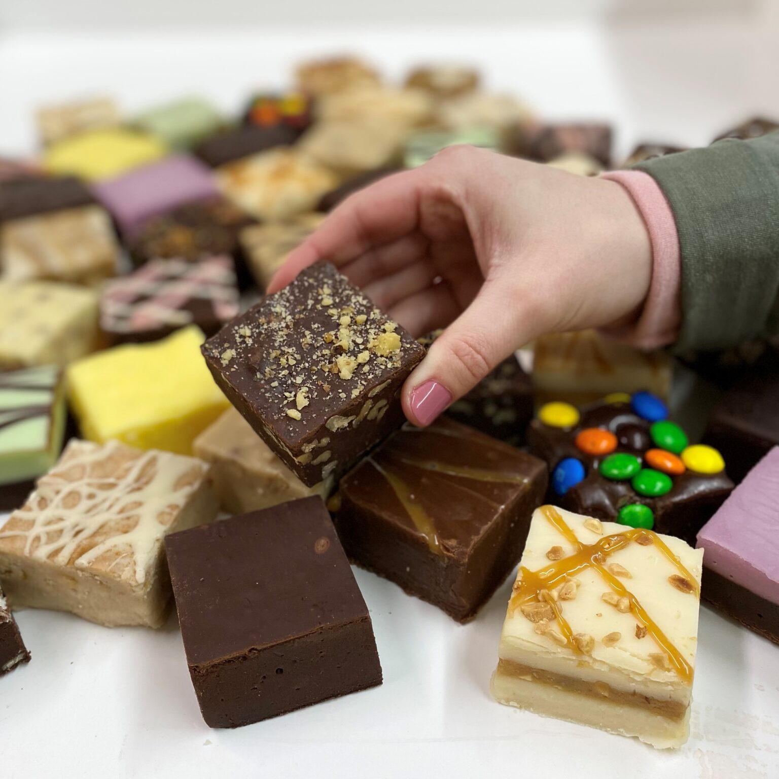 4 oz. piece of Chocolate Walnut Fudge in hand with assorted fudge pieces in the background.