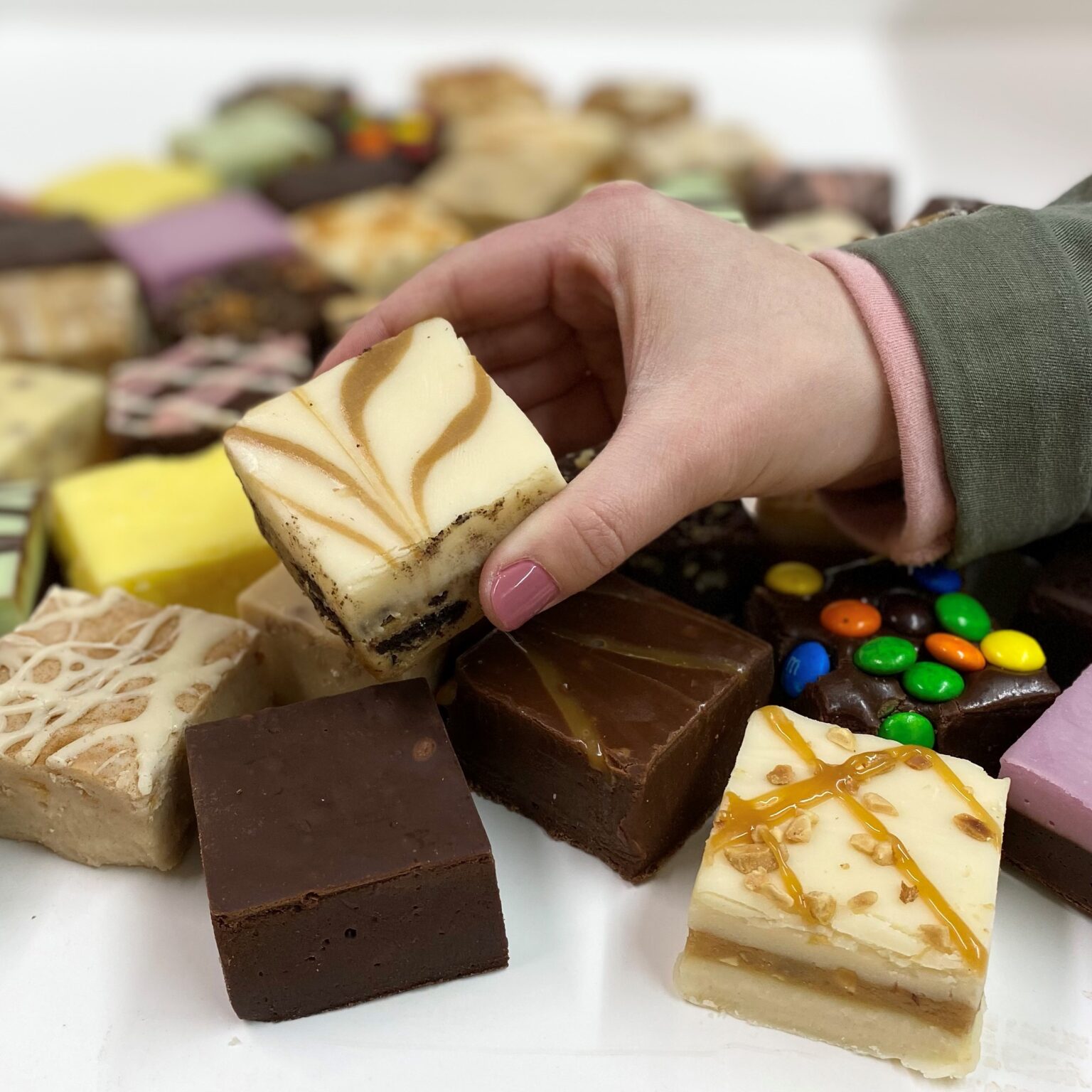 4 oz. piece of Coffee & Cookies Fudge in hand with assorted fudge pieces in the background.