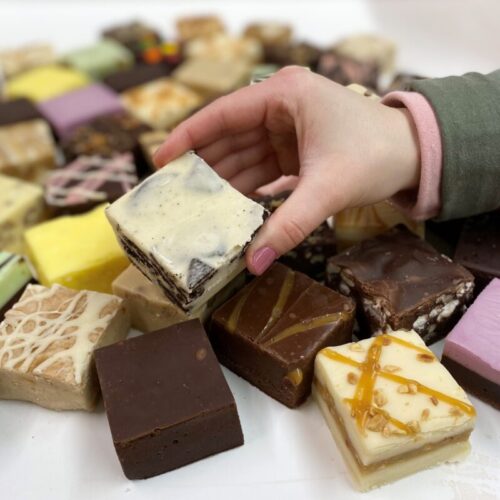 4 oz. piece of Cookies & Cream Fudge in hand with assorted fudge pieces in the background.