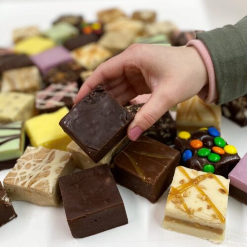 4 oz. piece of Dark Chocolate Fudge in hand with assorted fudge pieces in the background.