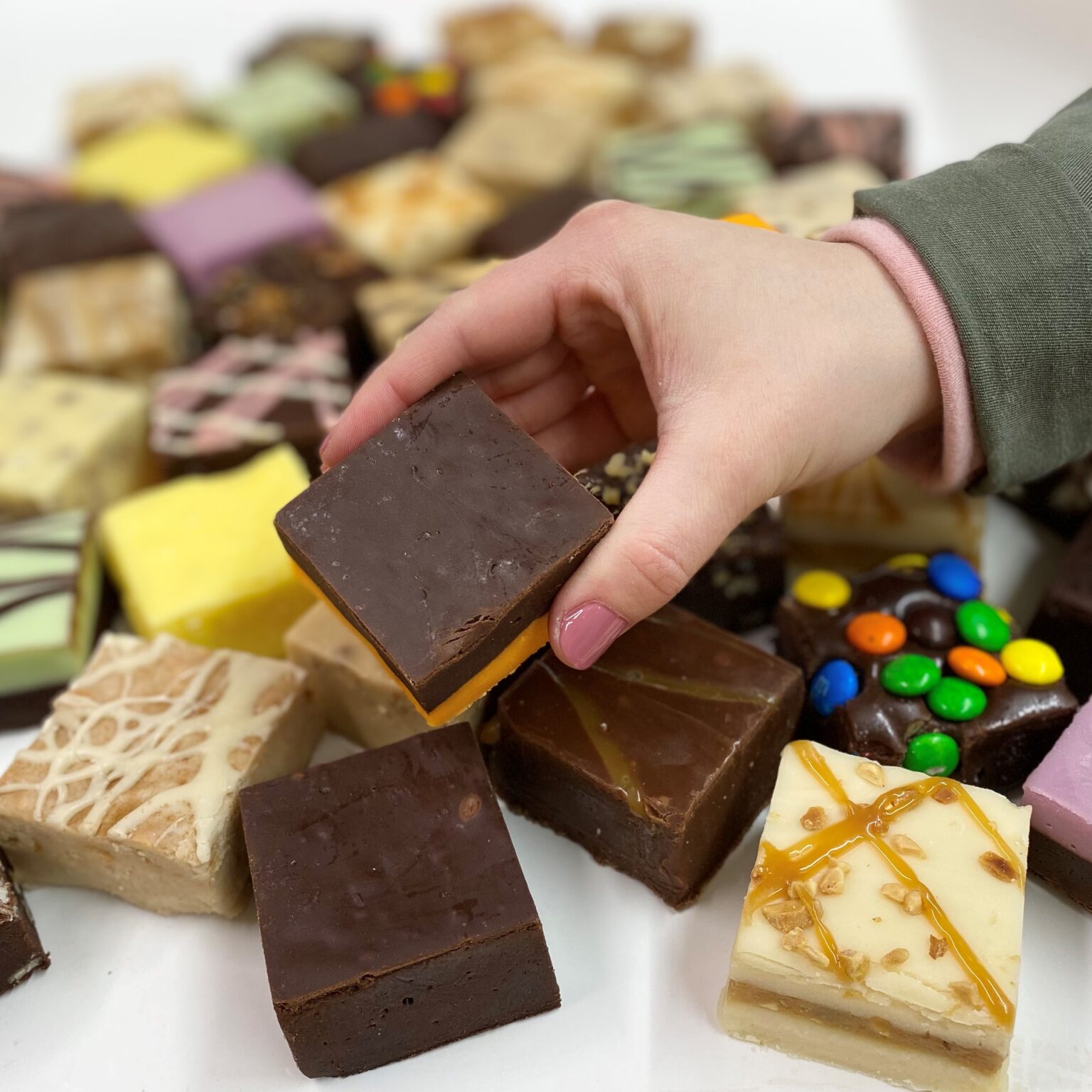 4 oz. piece of Dark Chocolate Orange Fudge in hand with assorted fudge pieces in the background.