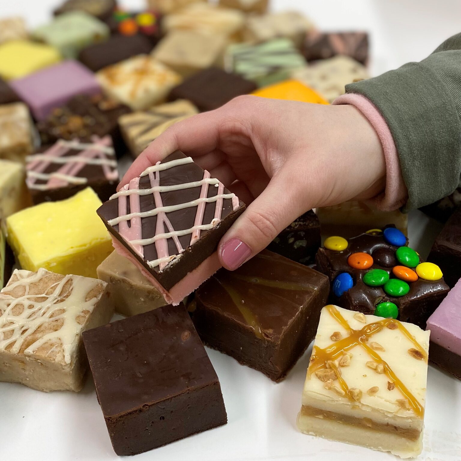 4 oz. piece of Dark Chocolate Raspberry Truffle Fudge in hand with assorted fudge pieces in the background.