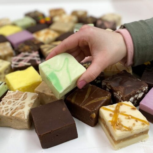 4 oz. piece of Dill Pickle Fudge in hand with assorted fudge pieces in the background.