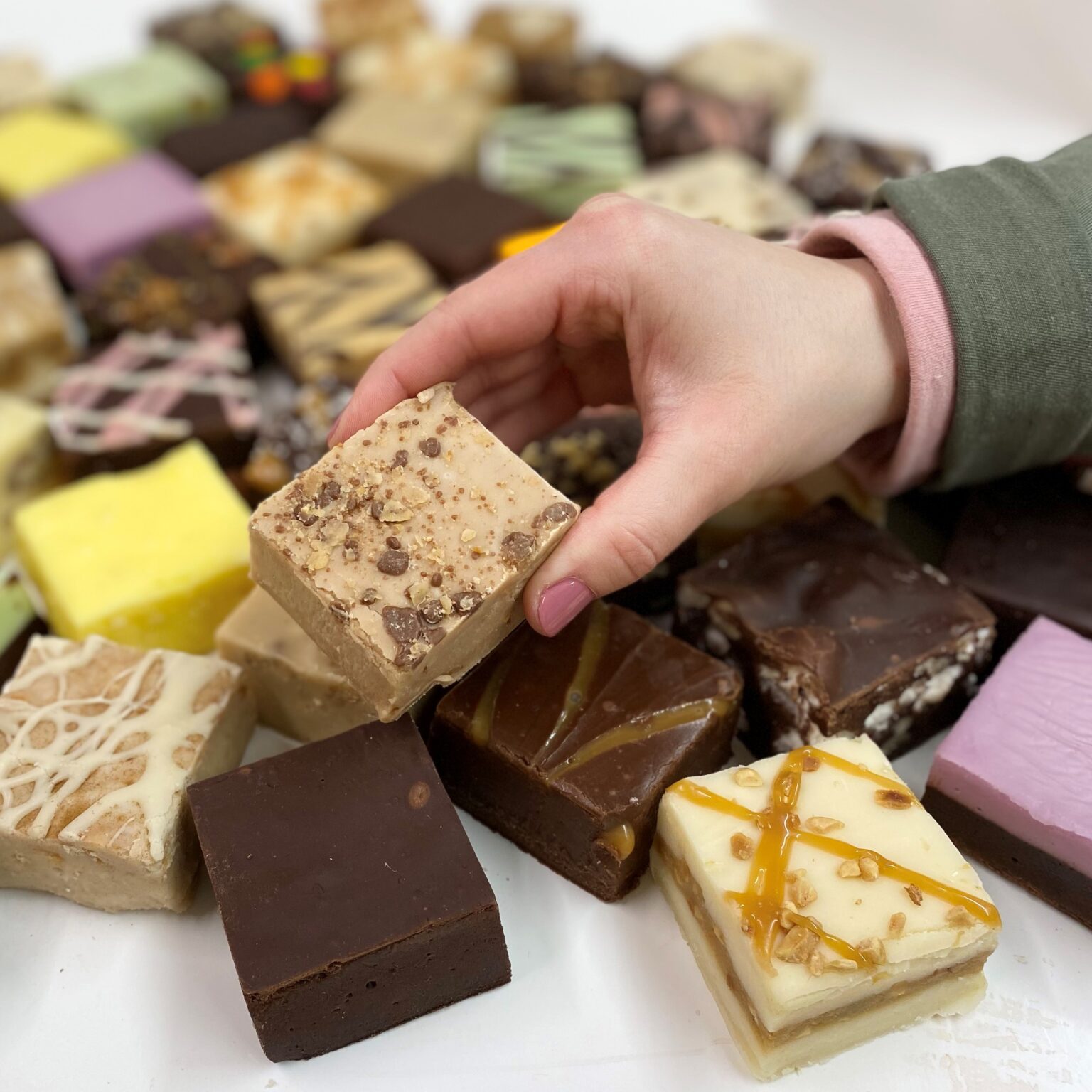 4 oz. piece of English Toffee Crunch Fudge in hand with assorted fudge pieces in the background.