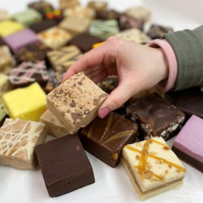 4 oz. piece of English Toffee Crunch Fudge in hand with assorted fudge pieces in the background.