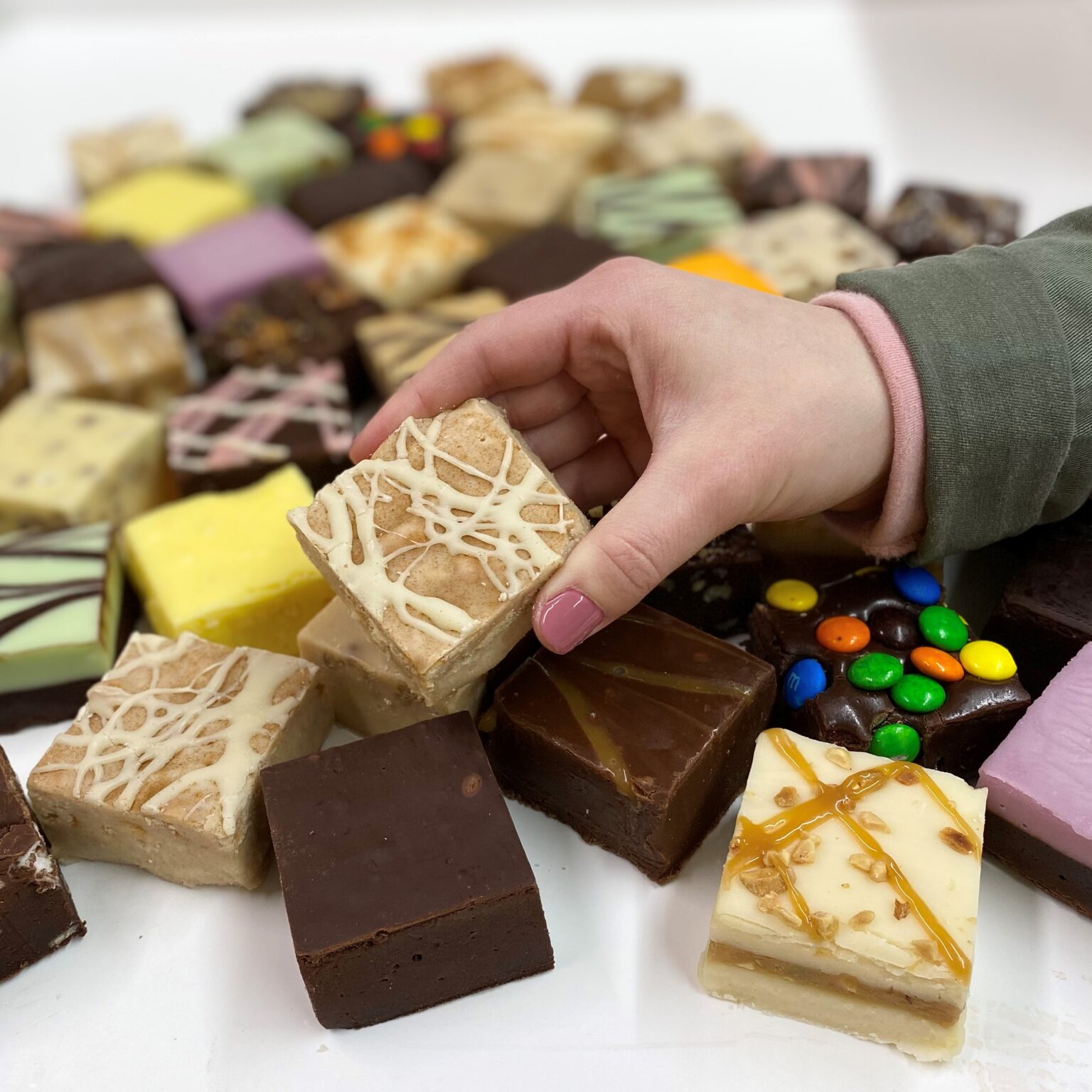 4 oz. piece of Iced Cinnamon Roll Fudge in hand with assorted fudge pieces in the background.