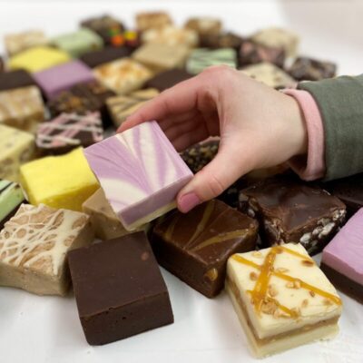 4 oz. piece of Lemon Lavender Fudge in hand with assorted fudge pieces in the background.