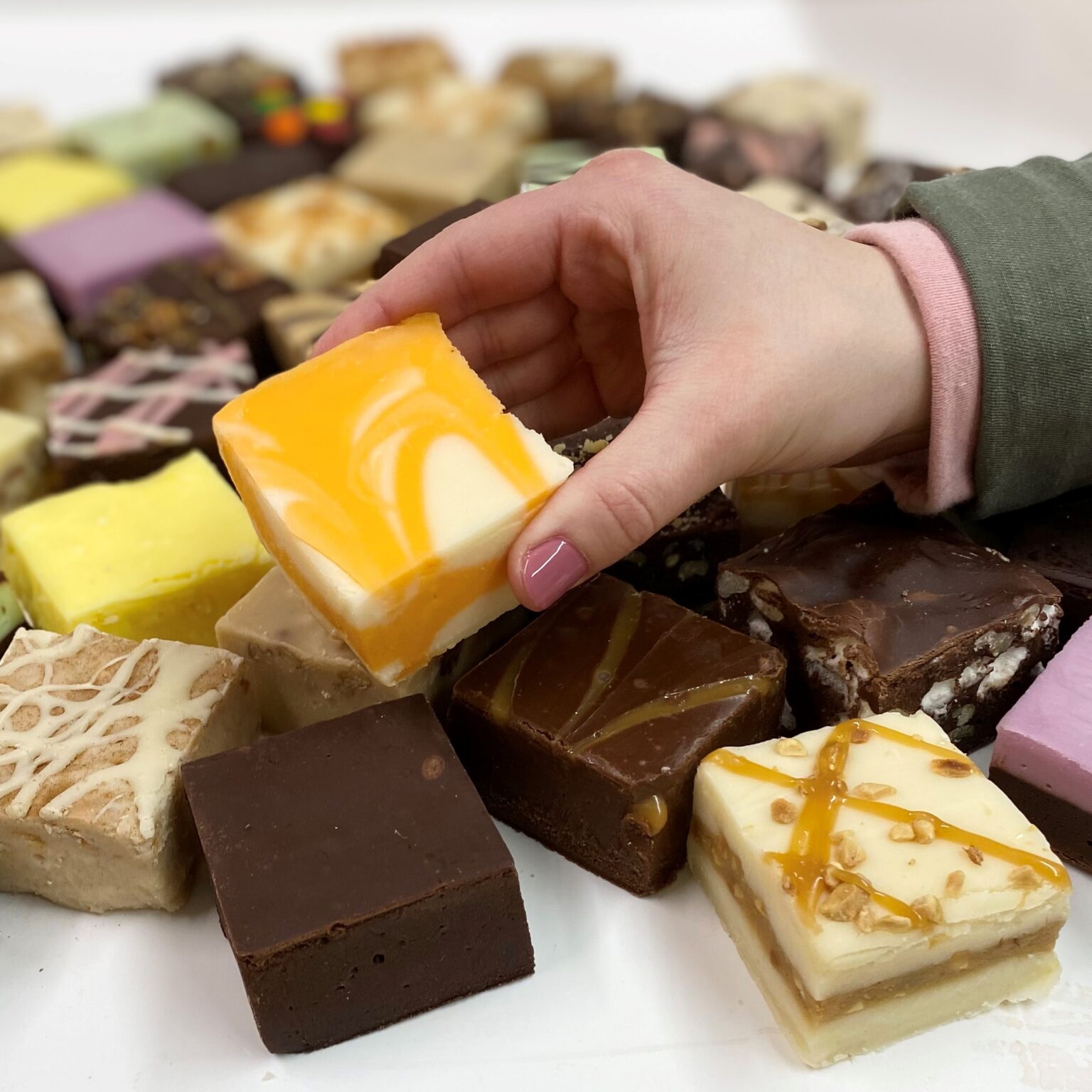 4 oz. piece of Orange Cream Fudge in hand with assorted fudge pieces in the background.