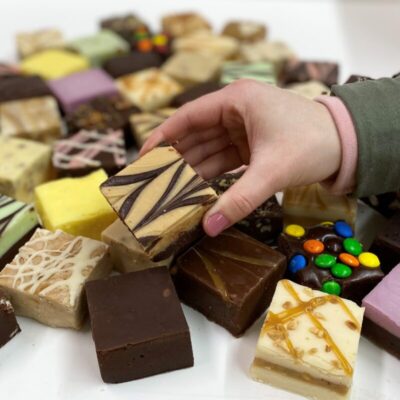 4 oz. piece of Peanut Butter Chocolate Fudge in Hand with assorted fudge pieces in the background.