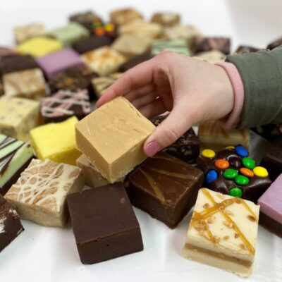4 oz. piece of Peanut Butter Fudge in Hand with assorted fudge pieces in the background.
