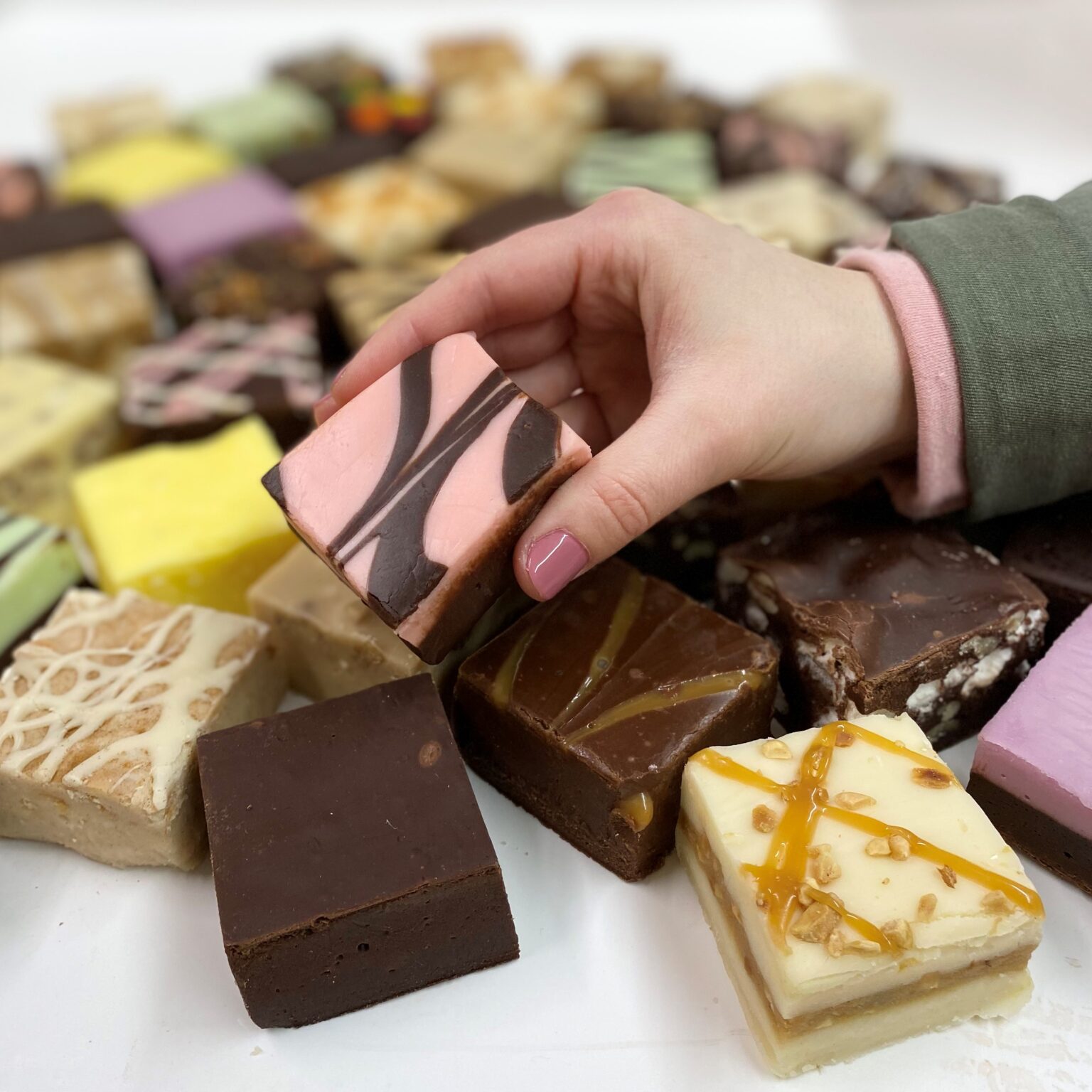 4 oz. piece of Raspberry Chocolate Swirl Fudge in Hand with assorted fudge pieces in the background.