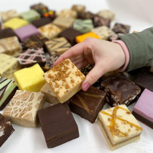 4 oz. piece of Salted Caramel Toffee Fudge in Hand with assorted fudge pieces in the background.