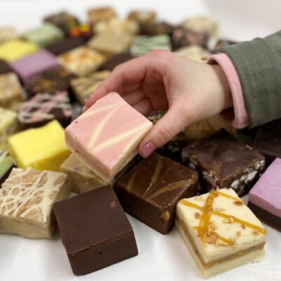 4 oz. piece of Strawberry Cheesecake Fudge in Hand with assorted fudge pieces in the background.
