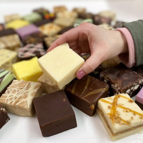 4 oz. piece of Vanilla Fudge in Hand with assorted fudge pieces in the background.