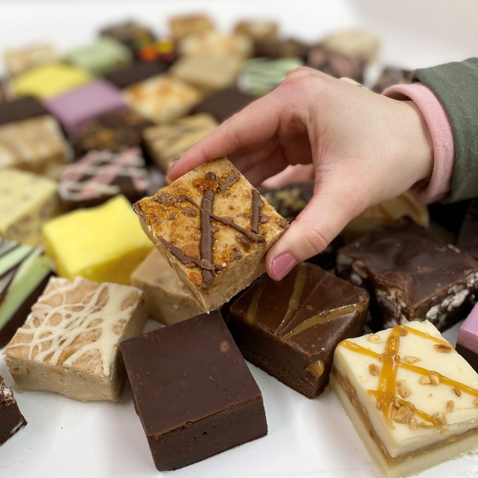 4 oz. piece of Vanilla Fudge with Butterfinger Pieces in Hand with assorted pieces in the background.