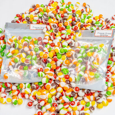 2 2.5 oz. bags of freeze dried skittles on top of an assortment of freeze dried skittles out of bag